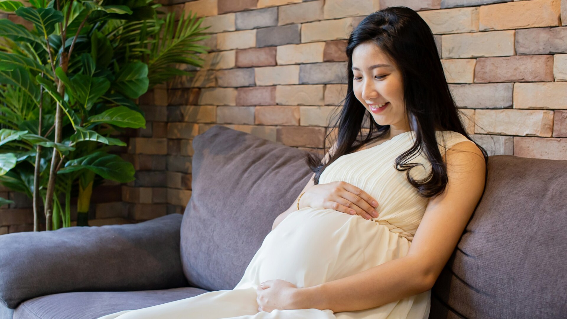 Happy Asian pregnant woman on couch